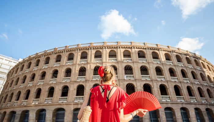 Woman traveling in Valencia city Woman in red dress with spanish hand fan stnading back in front of the bullring amphitheatre in Valencia city, Spain